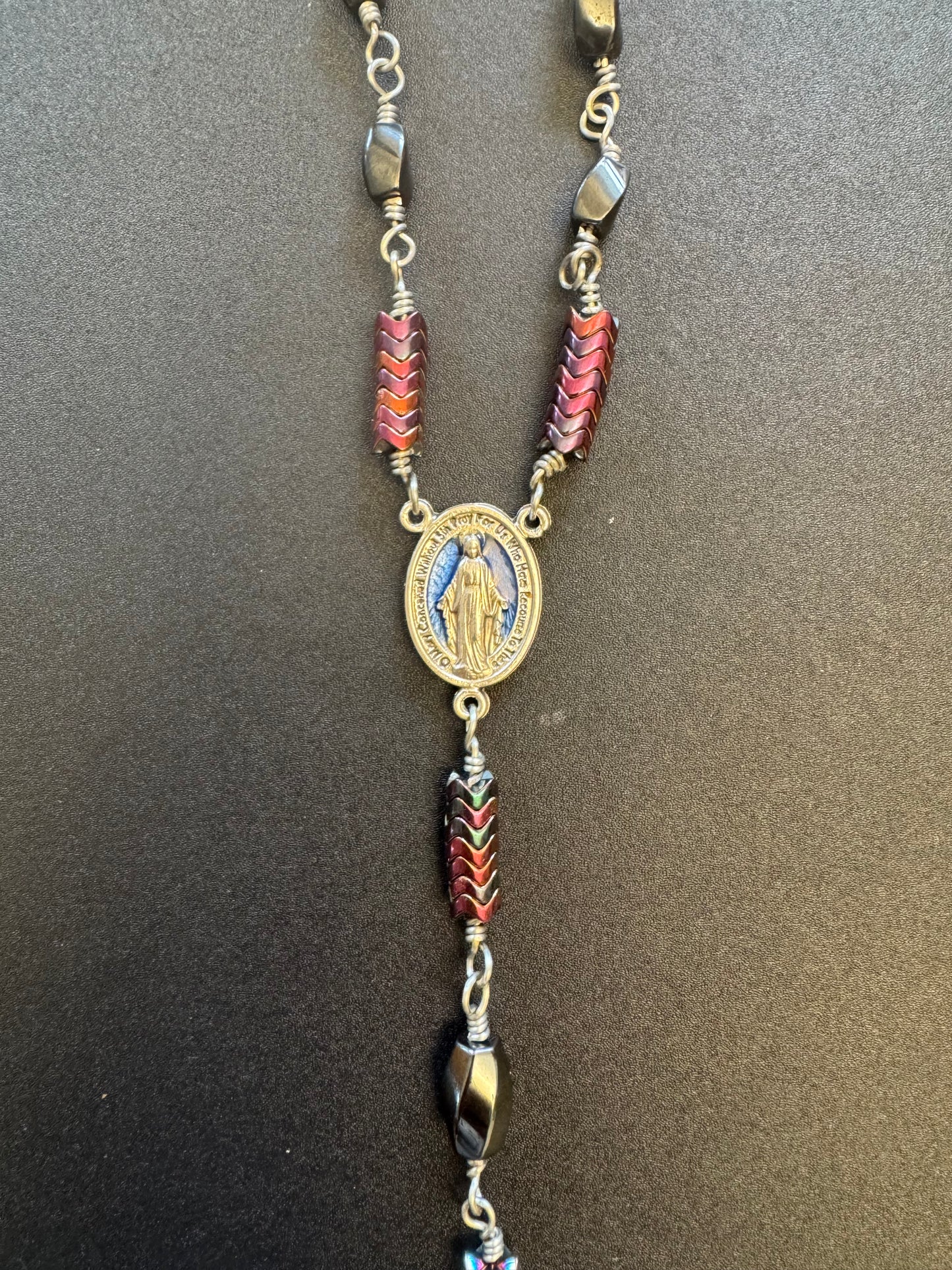 Closeup of blue miraculous medal centerpiece on single decade rosary with oval faceted hematite beads