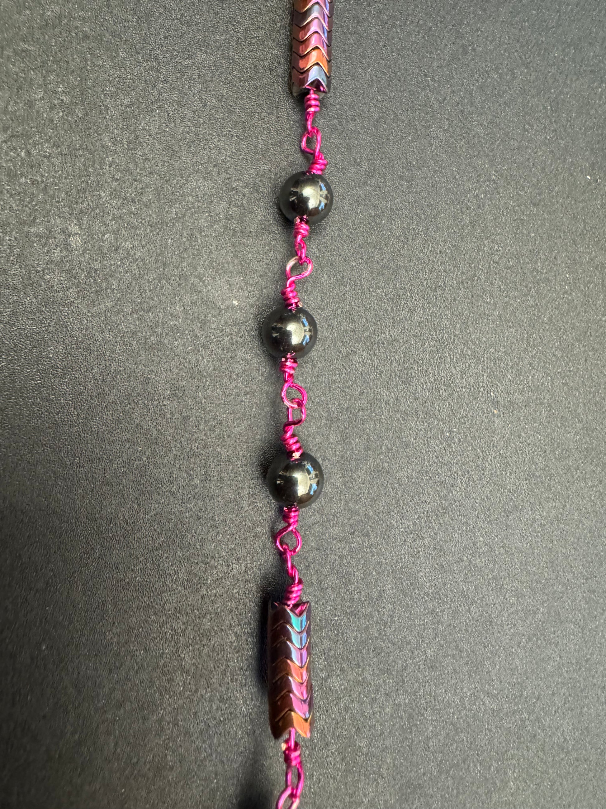 Closeup of full size rosary with hematite beads and fuchsia colored wire and miraculous medal centerpiece