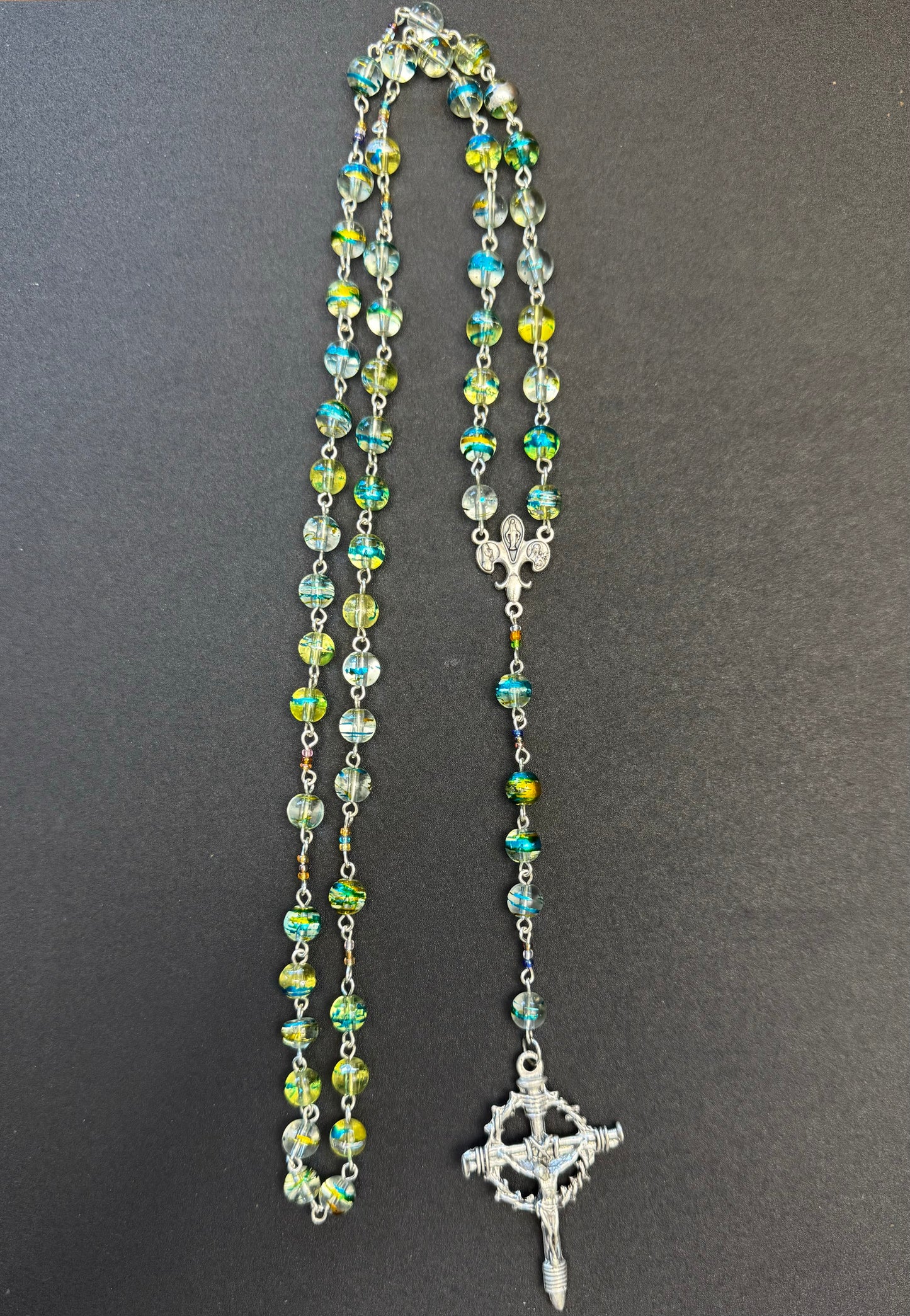 Zoom out of Blue and green swirl glass bead rosary with crown of thorns crucifix and fleur de lis centerpiece
