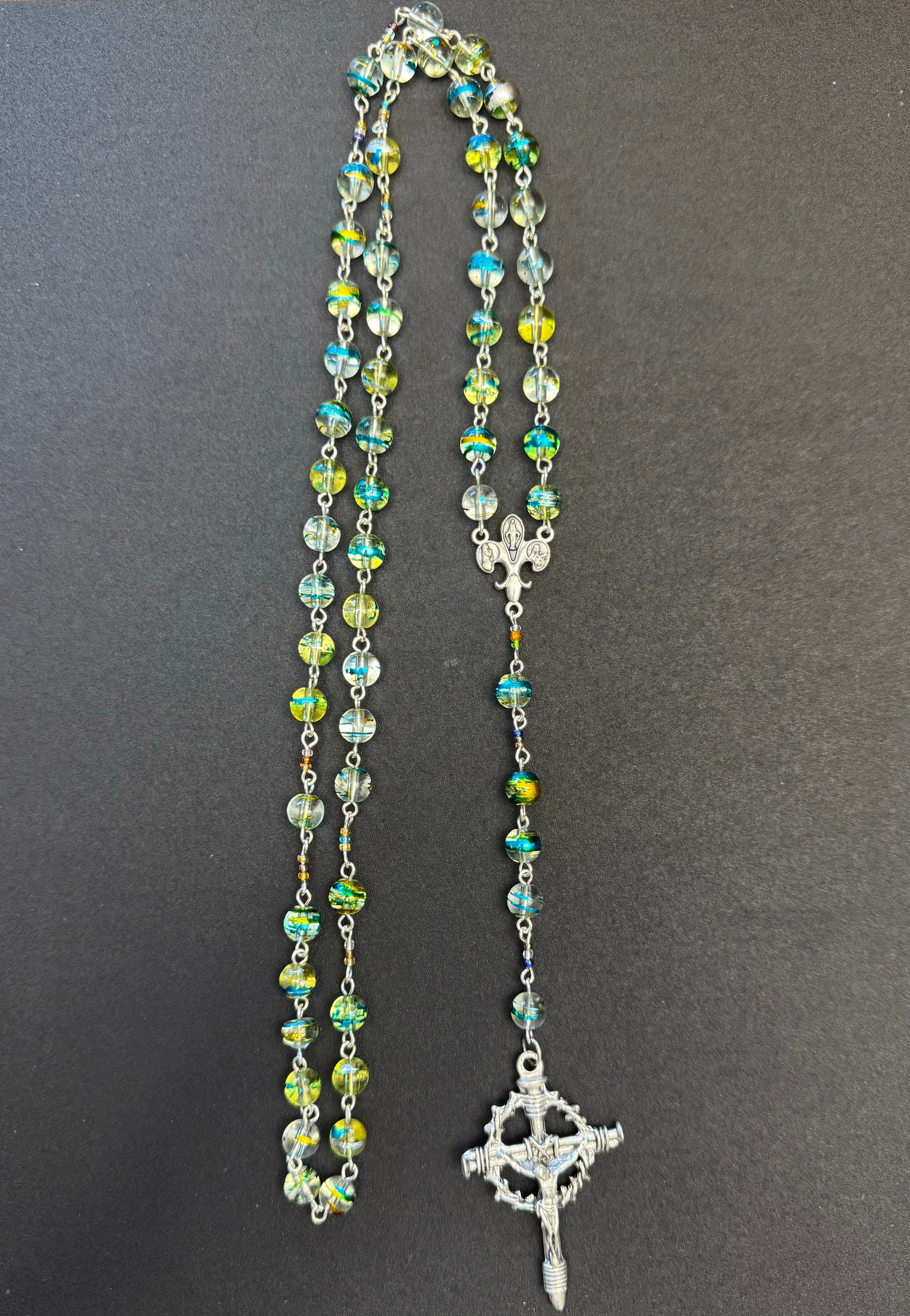 Zoom out of Blue and green swirl glass bead rosary with crown of thorns crucifix and fleur de lis centerpiece