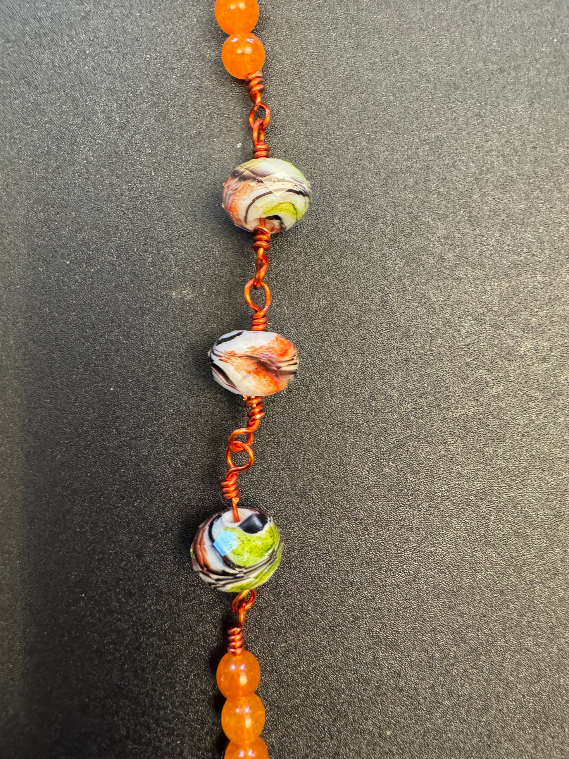 Closeup of single decade our lady of Guadalupe rosary with green and orange swirl glass beads and orange colored wire