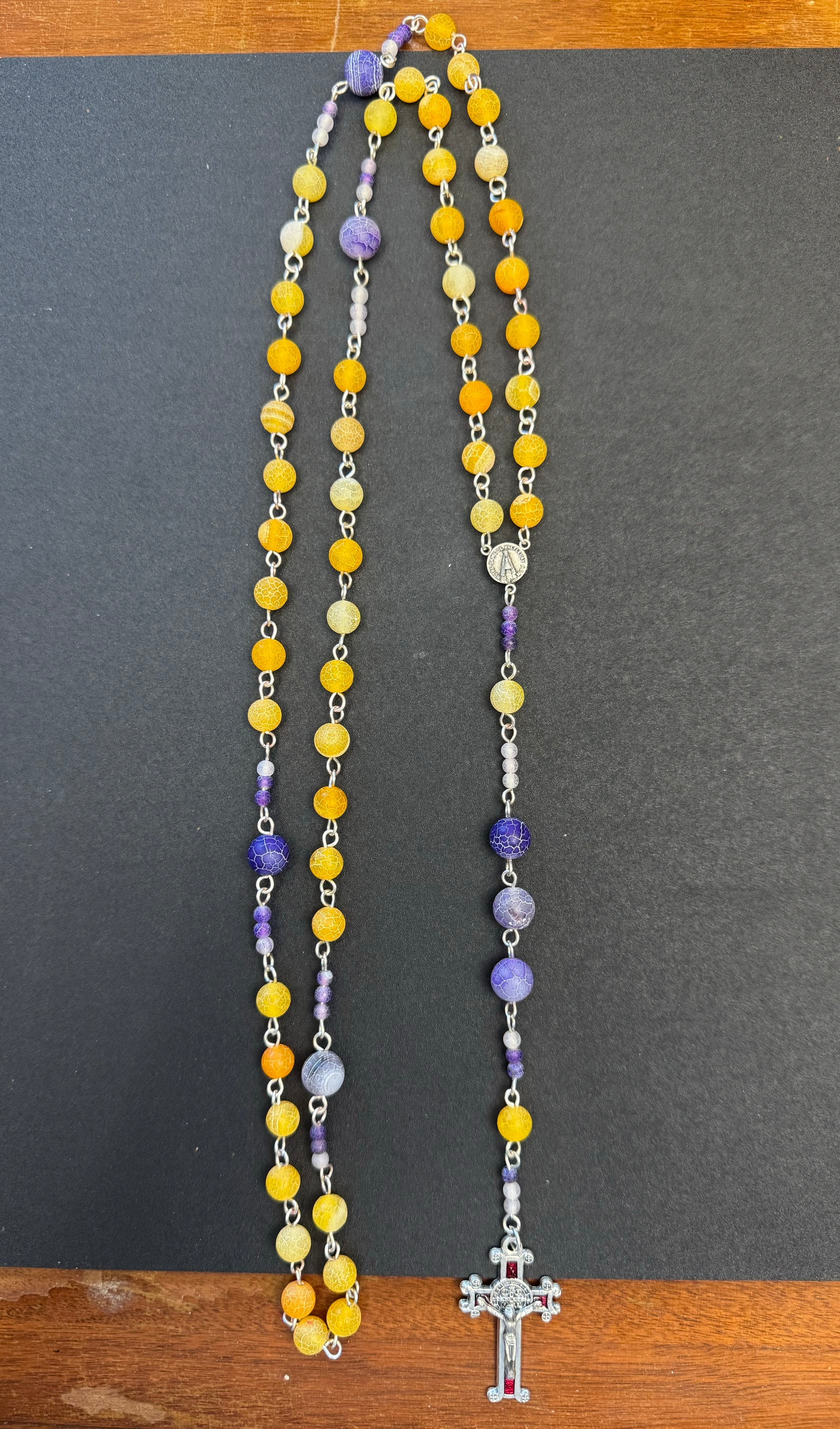zoomed out perspective of orange and purple frosted bead rosary with red crucifix