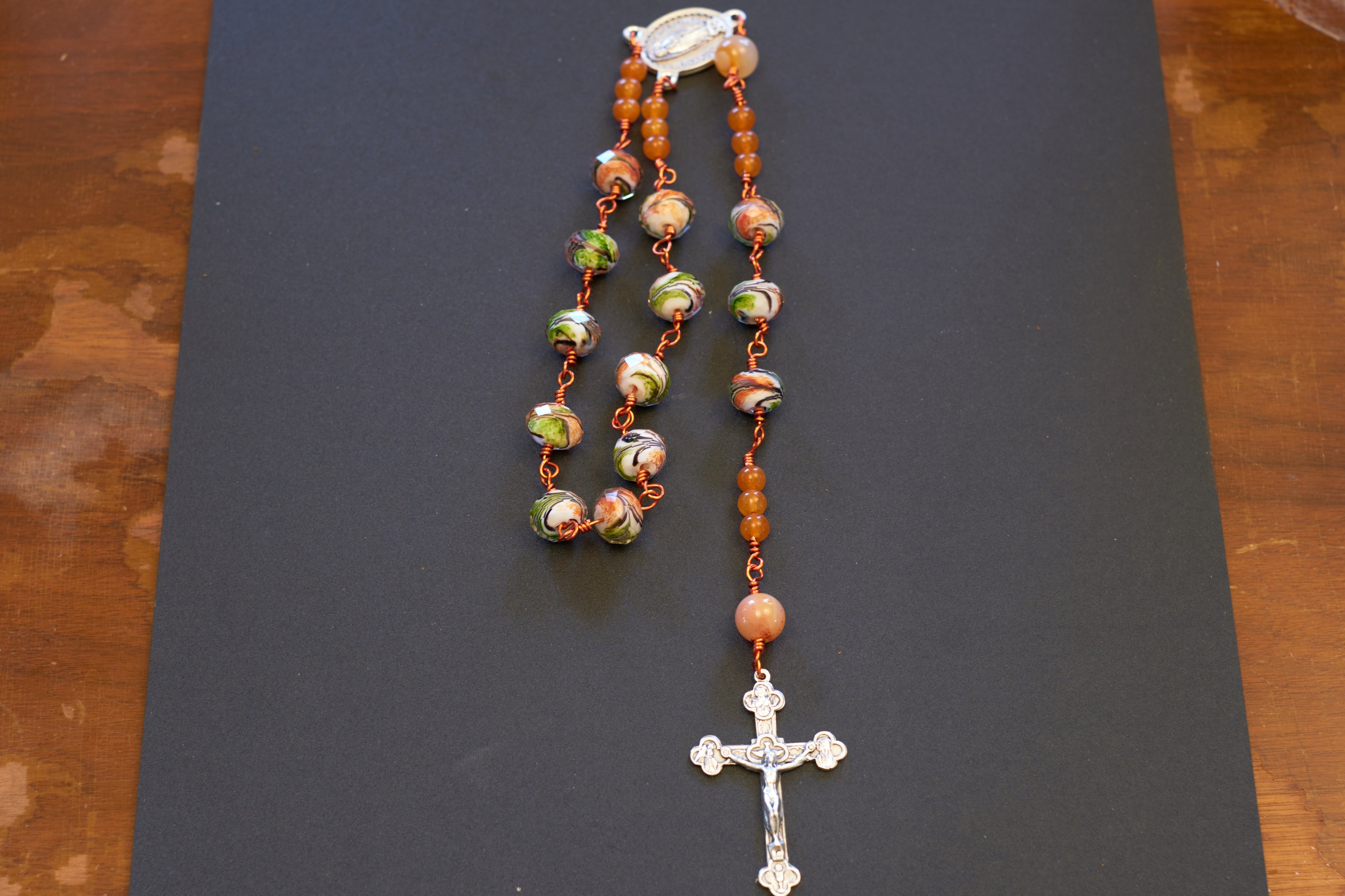 Closeup of single decade our lady of Guadalupe rosary with green and orange swirl glass beads and orange colored wire